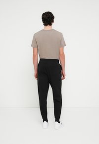 Μαύρο παντελόνι φόρμας με ελαστική μέση και πλαϊνές τσέπες, συνδυασμένο με κοντομάνικο λευκό t-shirt σε απόχρωση ταούπ, θέα από πίσω. Λευκά αθλητικά παπούτσια.