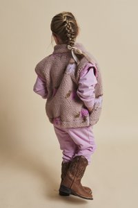 Vestă roz de fleece cu modele florale, purtată peste o bluză roz cu mâneci lungi și pantaloni asortați, combinată cu cizme maro de cowboy.