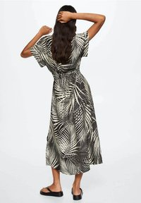 Zwart-witte jurk met palmbladpatroon, korte mouwen, getailleerde taille en een zwierige zoom, gecombineerd met platte zwarte sandalen.