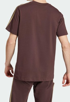 Camiseta de algodón marrón con mangas cortas, que presenta rayas doradas en los hombros. La tela es suave y tiene un corte holgado.