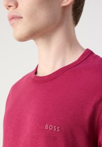 Piros crew-neck póló puha anyagból, finom textúrával és egy kis, dombornyomott "BOSS" logóval a bal mellrészen.
