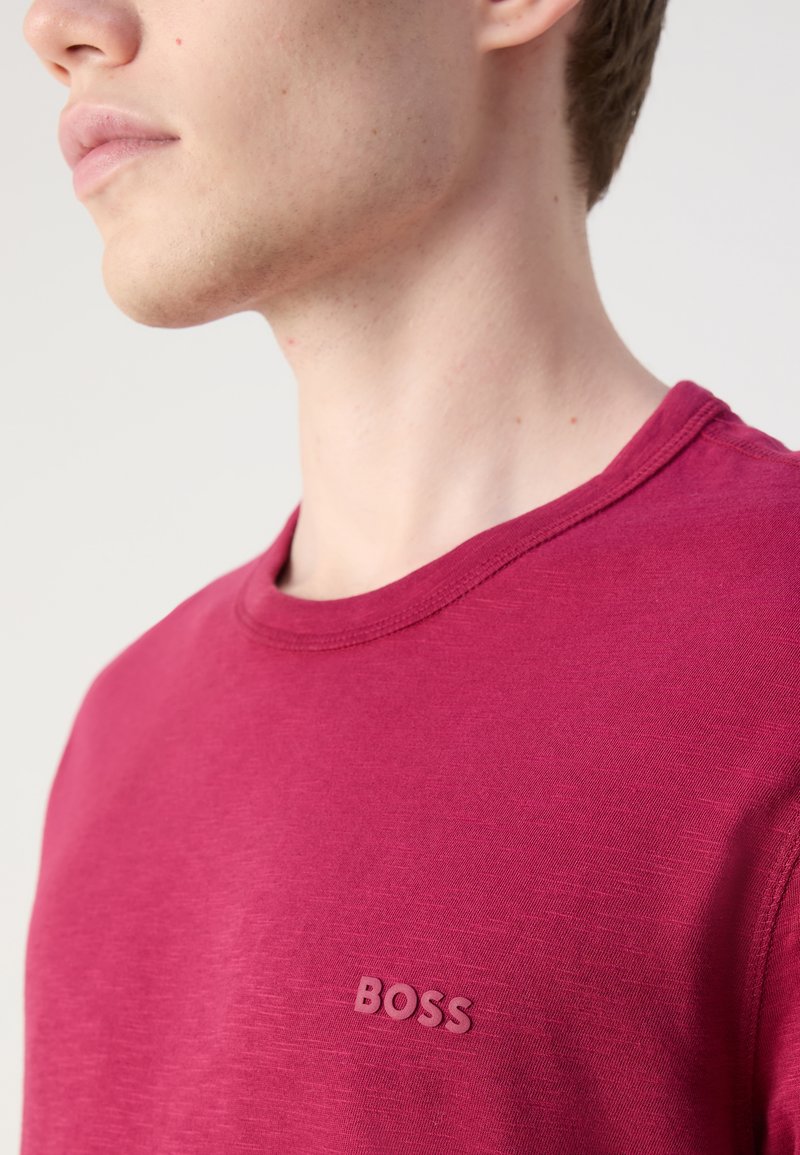 T-shirt rouge à col rond fabriquée en tissu doux, présentant une texture subtile et un petit logo "BOSS" en relief sur la partie gauche de la poitrine.