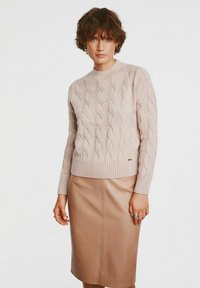 Jasnoróżowy sweter z dzianiny z wzorem w warkocze i ściągaczami, w połączeniu z dopasowaną beżową skórzaną spódnicą. Gładka tekstura i dopasowany krój.