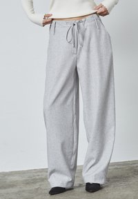 Grå bredbenede bukser med en struktureret stof, justerbar snor i taljen og dybe sidelommer, parret med sorte spidse sko.
