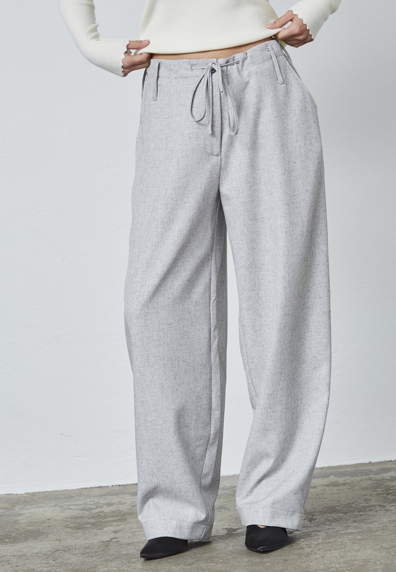 Grå bredbenede bukser med en struktureret stof, justerbar snor i taljen og dybe sidelommer, parret med sorte spidse sko.