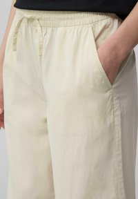 Lichtbeige wijde broek gemaakt van een zachte stof, met een elastische tailleband met een trekkoord en zijzakken. Gladde textuur.