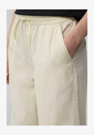 Jasno beżowe spodnie typu wide-leg wykonane z miękkiego materiału, z elastycznym paskiem w talii oraz sznurkiem i kieszeniami po bokach. Gładka struktura.