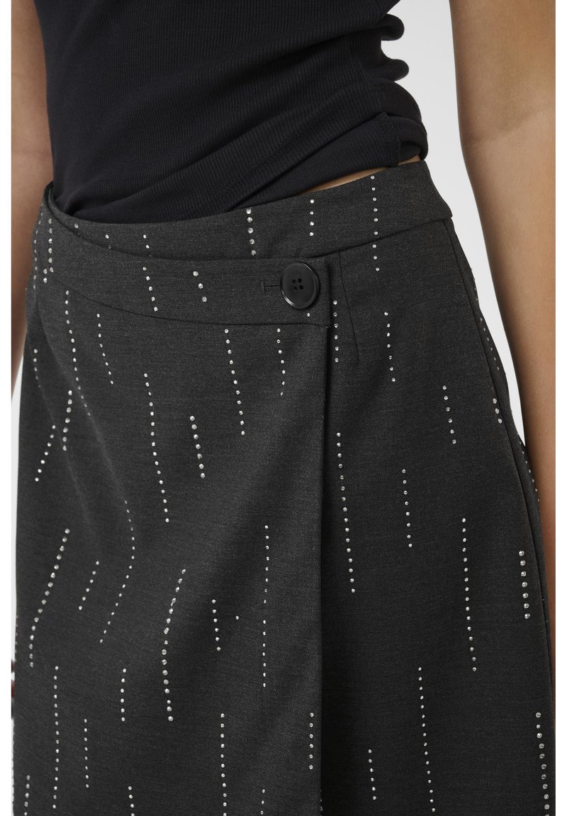 Gonna grigia con motivo verticale a pois argento, con pettinatura frontale e chiusura a bottone nero. Tessuto morbido e vestibilità a vita media.