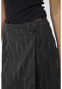 Szürke szoknya függőleges ezüst pöttyös mintával, ráncolt elülső résszel és fekete gombos záródással. Puha tapintású és közepes derékvonalú fazon.