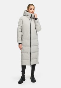 Cappotto lungo grigio chiaro imbottito con cappuccio, zip nere e tasche. Presenta un design trapuntato e si ferma sopra stivaletti neri alla caviglia.