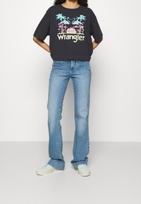 Sort kortærmet t-shirt med et farverigt grafisk design, parret med lyseblå flare-jeans og mintgrønne sneakers.