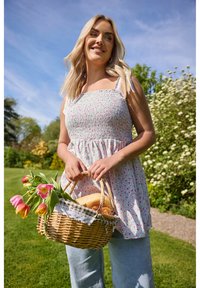 Vestido de verano con estampado floral y fruncido, con tirantes finos en colores claros, combinado con jeans de color azul claro. La persona sostiene una cesta de mimbre con tulipanes y pan.