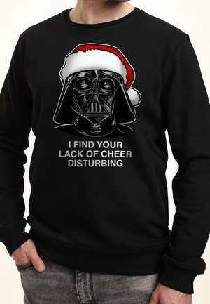 Sweat-shirt noir avec Dark Vador portant un chapeau de Père Noël et la phrase « Je trouve votre manque de joie inquiétant » en texte gris.