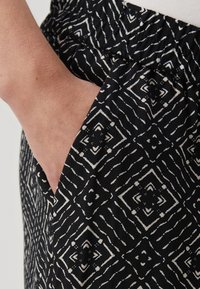 Crne hlače s geometrijskim uzorkom u bijeloj boji. Tkanina ima meku teksturu, elastičnu liniju struka i bočne džepove.
