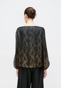 Schwarze transparente Bluse mit einem strukturierten Muster, ausgestattet mit langen Ärmeln und einem sanften orangefarbenen Farbverlauf am Saum. Glatter, leichter Stoff.