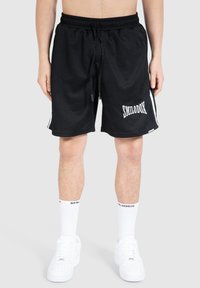Svarta sportshorts med ribbad textur, elastisk midja, dragsnör och vit "SMILODOX" logotyp, kombinerat med vita strumpor och skor.
