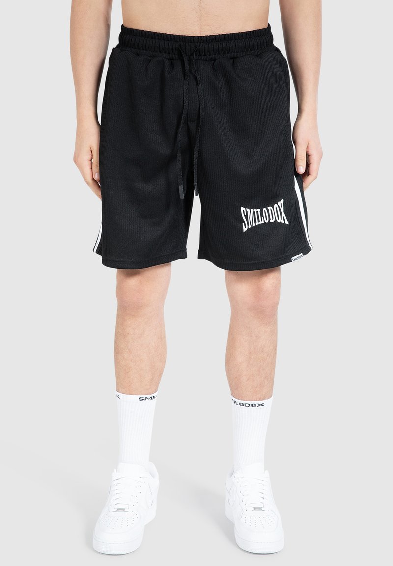 Svarta sportshorts med ribbad textur, elastisk midja, dragsnör och vit "SMILODOX" logotyp, kombinerat med vita strumpor och skor.