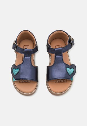 Sandales en cuir bleu marine avec une boucle, un design en T et un accent en cœur pailleté turquoise sur le côté extérieur. Semelle intérieure marron.