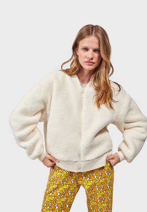 Veste bomber blanche, moelleuse, avec une fermeture éclair, un col rond et un ourlet côtelé. Assortie à un pantalon jaune vif avec un motif ludique.