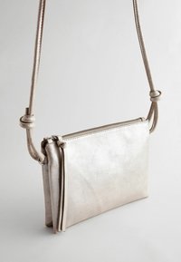 Piccola borsa a tracolla metallica argento con superficie testurizzata, chiusura con zip e dettaglio del manico annodato. Forma rettangolare compatta.