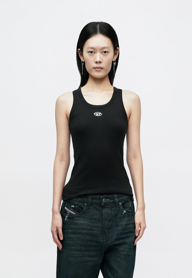 Fekete ujjatlan trikó kerek nyakkivágással és egy kis fehér logóval a mellkason, sötét farmernadrággal párosítva. Simább textúrájú.