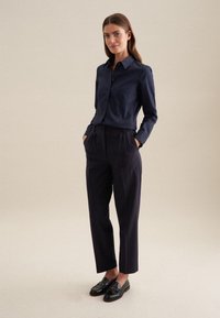 Marineblauwe button-up shirt met lange mouwen, gecombineerd met een hoge taille, donkere broek en zwarte loafers. Glad materiaal, getailleerde pasvorm, minimale details.