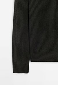 Pull côtelé foncé avec un motif en maille texturée. Le tissu est doux et extensible, avec des manches longues et un ourlet droit.