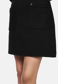 Black textured skirt featuring two large patch pockets, a straight cut, and a subtle geometric pattern, accented by a small metal button.