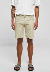 Shorts de mezclilla beige con un ajuste regular, diseño de cinco bolsillos, cierre frontal de botón y dobladillo cosido, combinados con sandalias deslizantes negras.