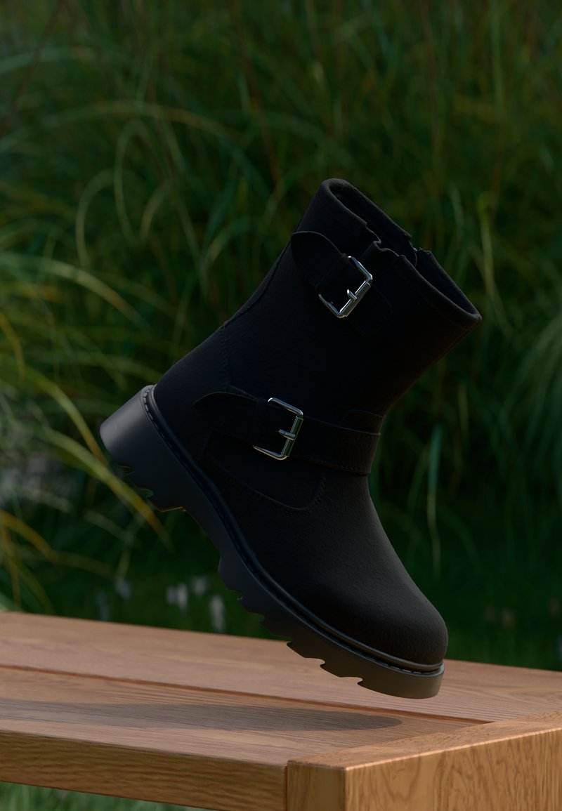 Botín negro de tobillo con hebillas, fabricado en material texturizado, con suela gruesa y diseño aerodinámico, sobre un fondo de vegetación natural.
