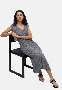 Vestido largo negro y blanco con un patrón, de mangas cortas, escote redondeado y un corte relajado, combinado con sandalias planas negras.
