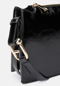 Čierna lakovaná crossbody taška so štruktúrovaným dizajnom, zlatými kovovými doplnkami a textúrovaným povrchom. Disponuje odnímateľným popruhom.