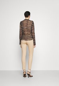 Sheer black blouse with striped pattern, paired with beige fitted pants and black heels. Blouse features long sleeves and a round neckline.