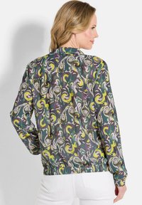 Bovenste bomberjack met patronen en draaidesigns in groene, gele en paarse tinten. Elastische taille en manchetten; lichtgewicht, gestructureerde stof.