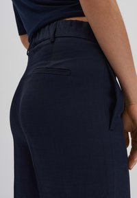 Marineblauwe broek met een elastische tailleband, zachte textuur en een zijzak. Het ontwerp heeft een gekleed uiterlijk aan de achterkant.