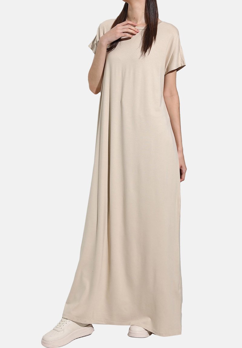 Robe maxi beige en tissu doux, avec une coupe décontractée, des manches courtes et un col rond, assortie à des baskets blanches.