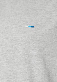 Gros plan sur un tissu gris clair avec une petite broderie rayée horizontale en blanc, bleu clair et bleu foncé centrée sur la surface.