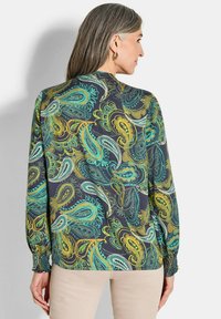 Langärmlige Bluse aus leichtem Stoff mit einem dunklen Hintergrund und einem lebhaften Paisley-Muster in Blaugrün und Gold. Geschwungene Manschetten sorgen für zusätzliche Details.
