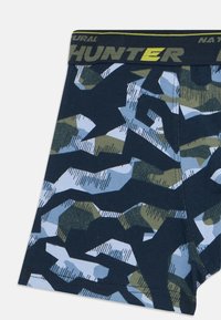 Boxer da uomo con motivo mimetico in verde, blu e nero, dotati di una vita nera con la scritta "HUNTER" in giallo e grigio.