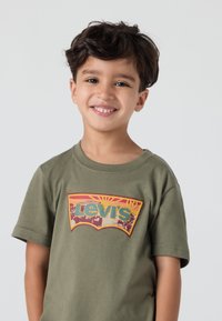 Alyvuogių žalios spalvos medvilnės marškinėliai su vintage Levi's logotipu geltonos ir raudonos spalvos, trumpomis rankovėmis ir apvaliu iškirpimu.