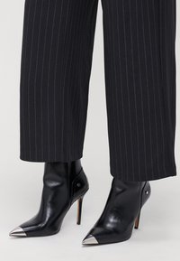 Schwarze Leder-Ankelstiefel mit spitzen Zehen und metallischen silbernen Akzenten. Stiletto-Absätze und dezente Nahtdetails ergänzen ein elegantes Design.