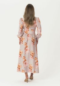 Lange bloemenjurk van lichtroze stof, met pofmouwen, eenGathered taille en een volle rok met perzik- en oranje bloemenpatronen.