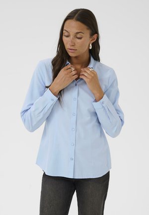 Light blue button-up shirt made of smooth fabric, featuring a classic collar, long sleeves, and a curved hemline with subtle button detail.