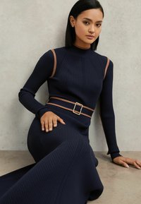 Marineblauwe jurk van geribbelde stof met lange mouwen, met beige schouderaccenten en een bijpassende riem met een vierkante gesp, ontwerp tot op de grond.