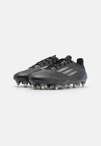 Sorte fotballsko med teksturert overflate, med sølvfargete detaljer, en strømlinjeformet design og spisse pigger for godt grep.