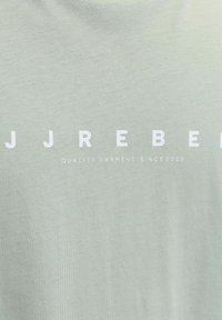 Tissu gris clair avec grand texte blanc "JJ REBEL" et texte plus petit en dessous indiquant "VÊTEMENT DE QUALITÉ DEPUIS 2023."
