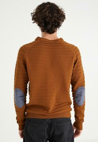 Suéter de punto marrón texturizado con un cuello alto y parches azules en los codos, que presenta un diseño entallado y puños y dobladillo acanalados.