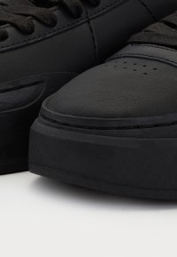 Μαύρες πλατφόρμες αθλητικά παπούτσια με παχιές σόλες, υφή από δέρμα και μαύρα κορδόνια σε λευκή επιφάνεια.