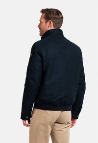 Navy blue bomber jacket in textured fabric with a high collar, ribbed cuffs, and a fitted waistband. Features button accents on the sleeves.