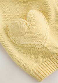 Rumena pletena majica z velikim našitim srcem. Rebrasti manšeti in natančno šivanje okoli srca dodajata teksturo.